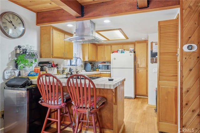 kitchen featuring island range hood, kitchen peninsula, white fridge, beamed ceiling, and light hardwood / wood-style floors