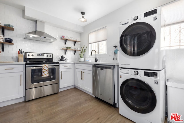 kitchen featuring tasteful backsplash, white cabinets, stacked washer / drying machine, stainless steel appliances, and wall chimney exhaust hood