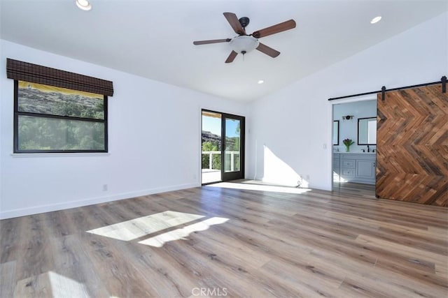 empty room with vaulted ceiling, a barn door, hardwood / wood-style floors, and ceiling fan