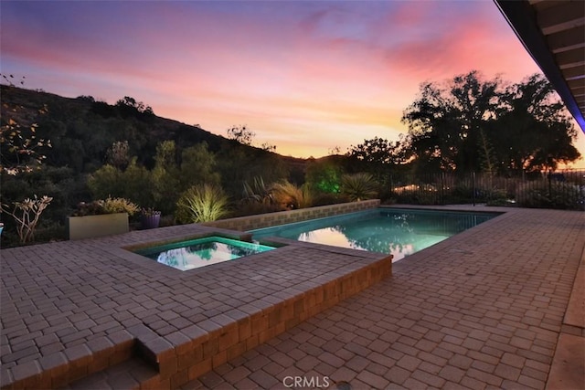 pool at dusk with an in ground hot tub and a patio area