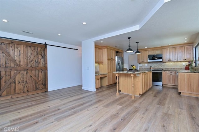 kitchen with a center island, a barn door, hanging light fixtures, light hardwood / wood-style flooring, and stainless steel appliances