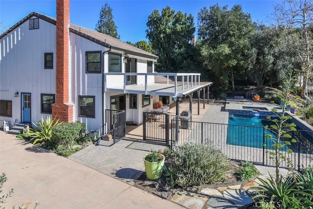 rear view of property featuring a pool with hot tub, a balcony, and a patio