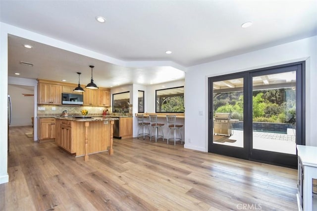 kitchen with appliances with stainless steel finishes, decorative light fixtures, light wood-type flooring, a kitchen bar, and a kitchen island