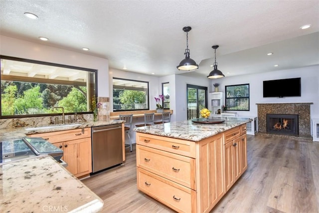 kitchen featuring a center island, light hardwood / wood-style floors, hanging light fixtures, stainless steel dishwasher, and sink