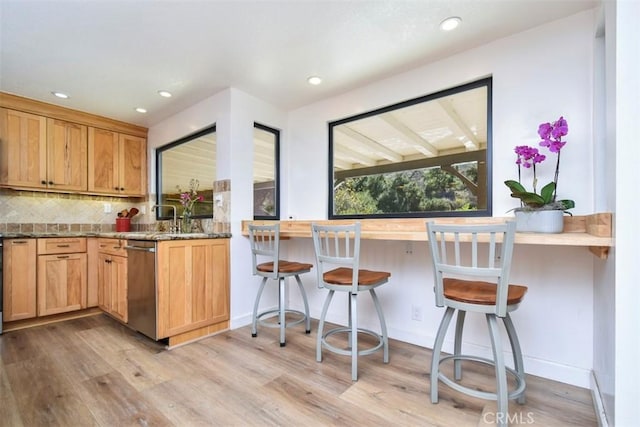 kitchen featuring light stone countertops, a kitchen bar, backsplash, stainless steel dishwasher, and light hardwood / wood-style flooring