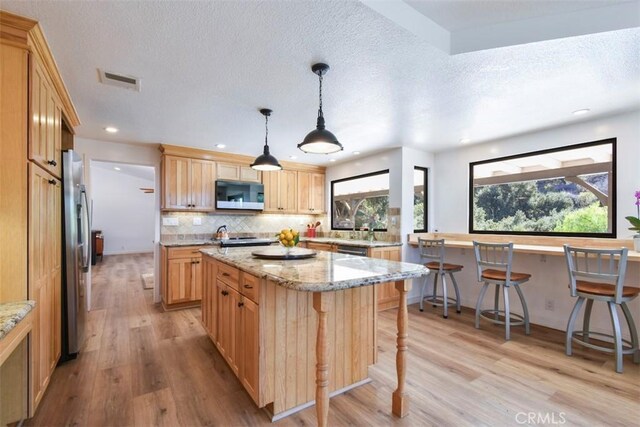 kitchen featuring light stone countertops, hanging light fixtures, light wood-type flooring, a breakfast bar area, and stainless steel fridge