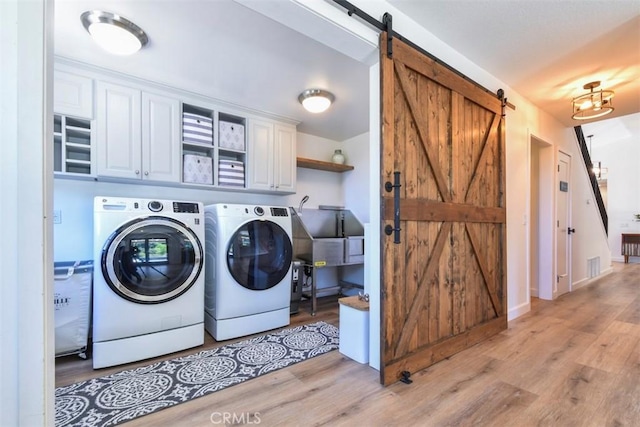 laundry area featuring washing machine and dryer, light wood-type flooring, a barn door, and cabinets