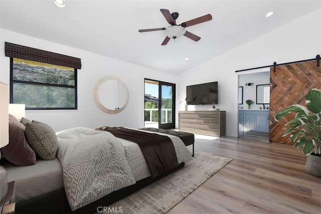 bedroom featuring lofted ceiling, wood-type flooring, ceiling fan, ensuite bathroom, and a barn door