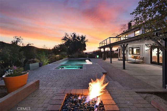 pool at dusk featuring an in ground hot tub, an outdoor fire pit, and a patio area