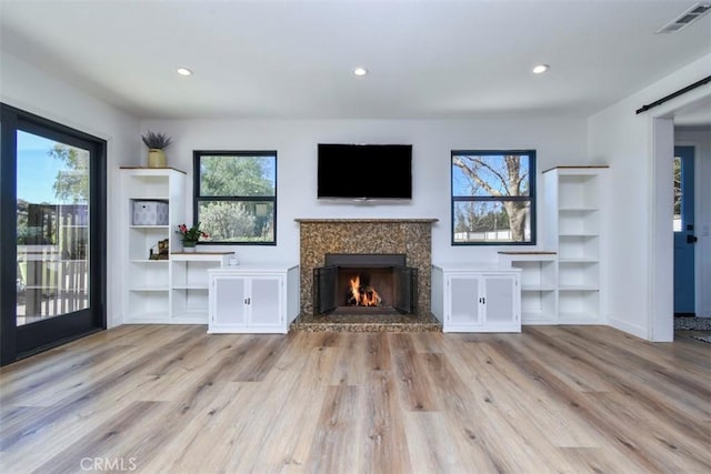 unfurnished living room featuring a fireplace, light hardwood / wood-style flooring, and a barn door