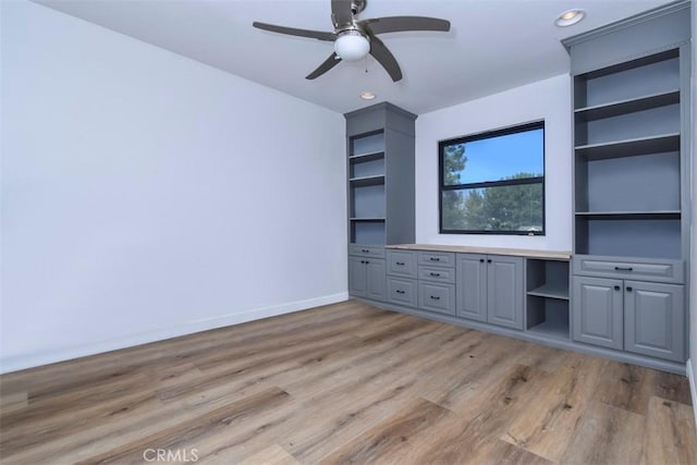 unfurnished living room with built in shelves, light wood-type flooring, and ceiling fan