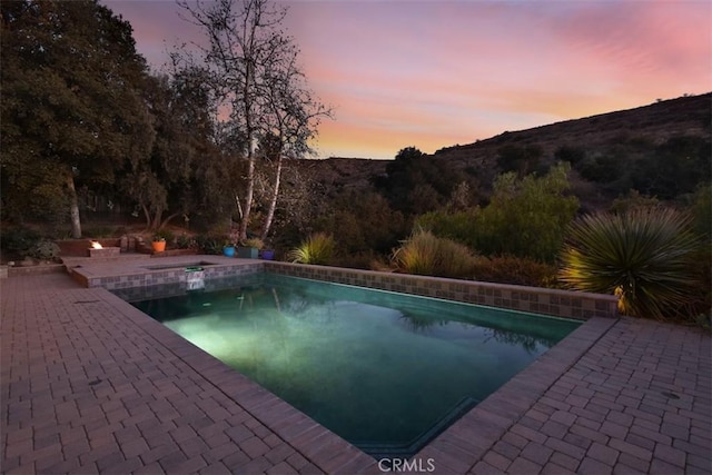 pool at dusk featuring a mountain view and a patio