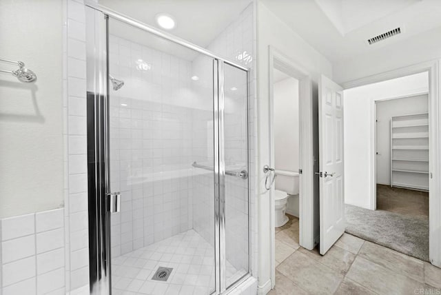 bathroom featuring toilet, a shower with door, and tile patterned flooring