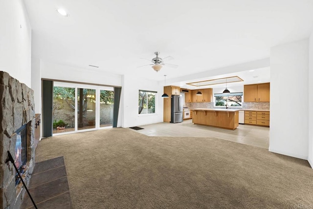 unfurnished living room featuring ceiling fan, light carpet, and a stone fireplace