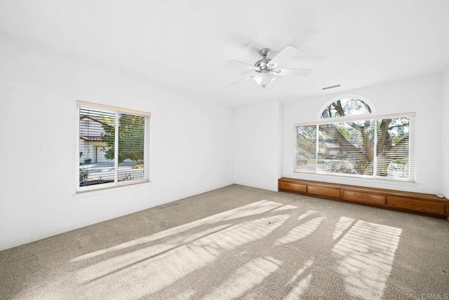 carpeted spare room with ceiling fan and plenty of natural light