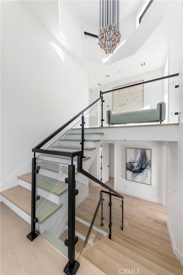 stairs with hardwood / wood-style flooring, a towering ceiling, and an inviting chandelier