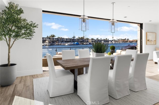 dining space featuring light wood-type flooring, a water view, and floor to ceiling windows