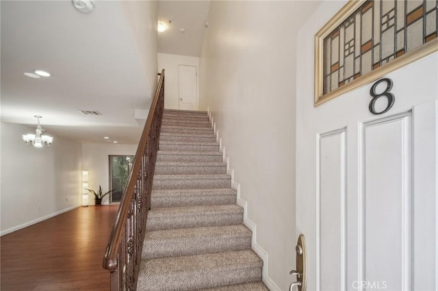 stairs with hardwood / wood-style floors and a chandelier