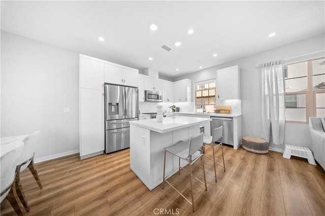 kitchen with light hardwood / wood-style floors, white cabinets, a kitchen island, a breakfast bar, and stainless steel appliances