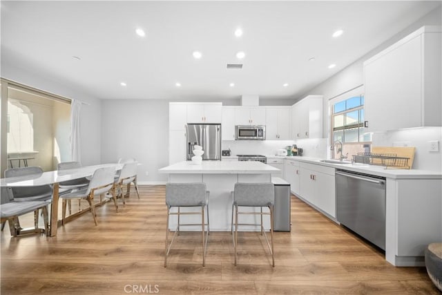 kitchen with white cabinetry, sink, a kitchen island, light hardwood / wood-style flooring, and stainless steel appliances