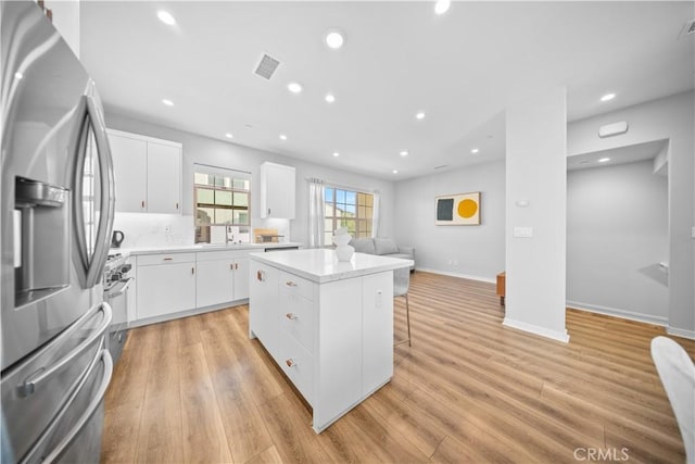 kitchen with a kitchen island, a kitchen bar, white cabinetry, light hardwood / wood-style floors, and stainless steel fridge with ice dispenser