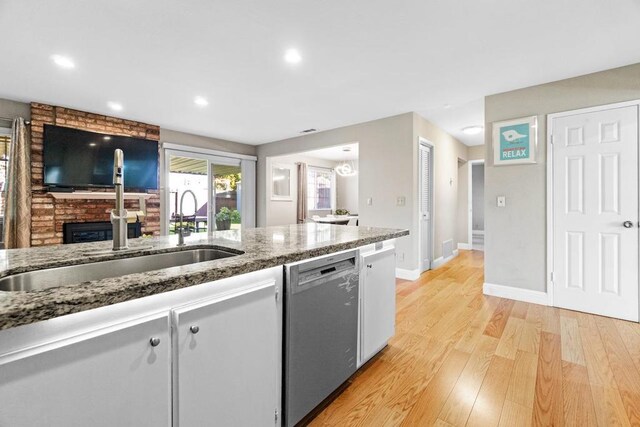 kitchen featuring sink, light hardwood / wood-style flooring, dishwasher, dark stone counters, and a fireplace