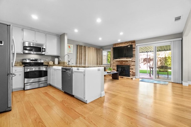 kitchen with white cabinetry, a brick fireplace, light wood-type flooring, appliances with stainless steel finishes, and kitchen peninsula