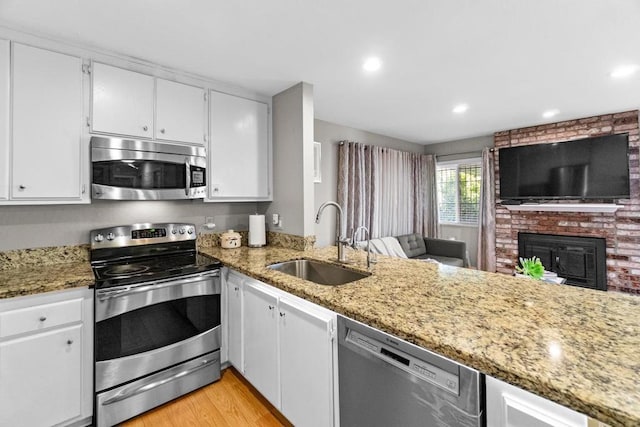 kitchen featuring appliances with stainless steel finishes, stone countertops, a fireplace, white cabinetry, and sink