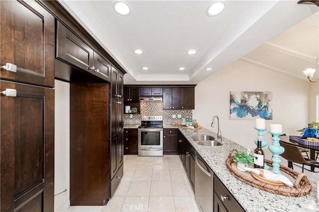 kitchen with light stone countertops, stainless steel appliances, sink, a tray ceiling, and dark brown cabinets