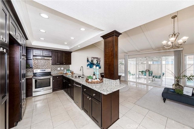 kitchen with appliances with stainless steel finishes, sink, a raised ceiling, kitchen peninsula, and decorative columns