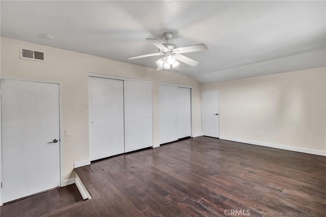 unfurnished bedroom featuring dark hardwood / wood-style floors, two closets, and ceiling fan