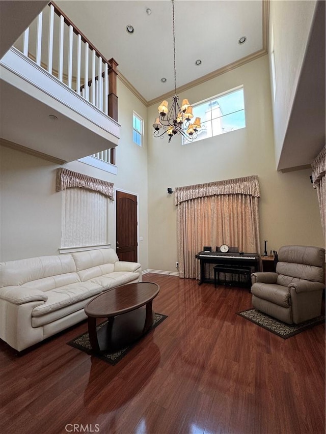 living room with dark wood-type flooring, a high ceiling, ornamental molding, and an inviting chandelier