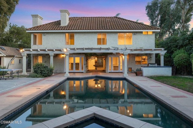 back house at dusk with exterior kitchen, a patio, a pool with hot tub, and a pergola