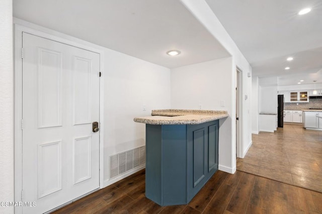 kitchen featuring dark hardwood / wood-style flooring, backsplash, white cabinets, and black fridge