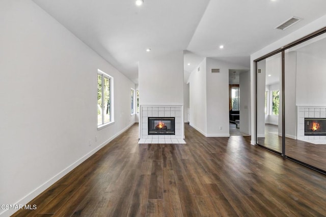 unfurnished living room with a tiled fireplace, lofted ceiling, dark hardwood / wood-style floors, and a healthy amount of sunlight