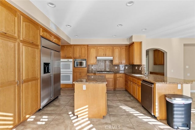 kitchen featuring stone countertops, appliances with stainless steel finishes, a center island, and sink