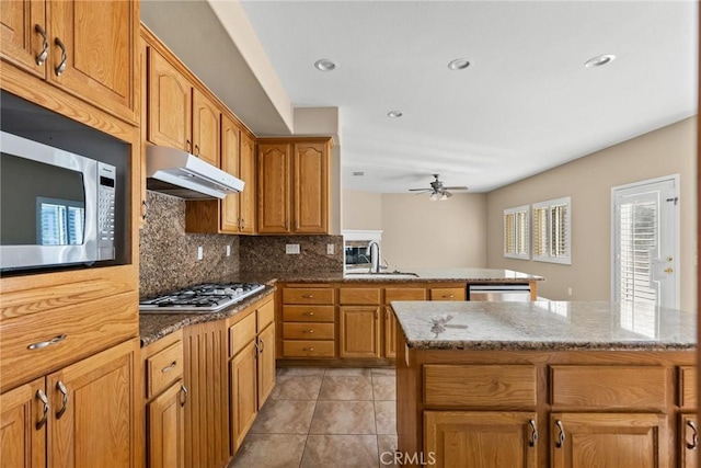 kitchen with sink, appliances with stainless steel finishes, a kitchen island, light stone countertops, and backsplash