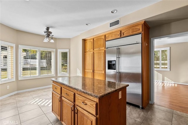 kitchen with light tile patterned floors, a center island, stainless steel built in refrigerator, a wealth of natural light, and dark stone counters