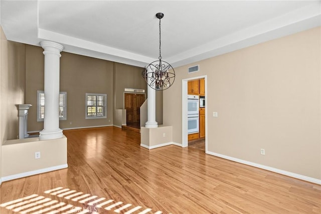 unfurnished living room featuring a chandelier, hardwood / wood-style floors, and ornate columns