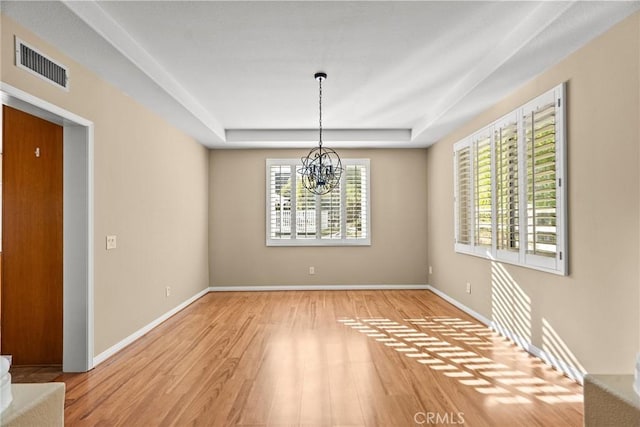 unfurnished dining area featuring a notable chandelier, a raised ceiling, light hardwood / wood-style flooring, and a wealth of natural light