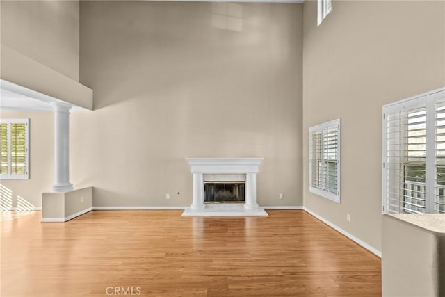 unfurnished living room featuring a towering ceiling, light wood-type flooring, and ornate columns