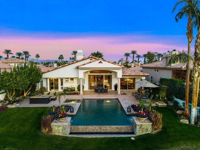 back house at dusk featuring a patio, a lawn, and outdoor lounge area