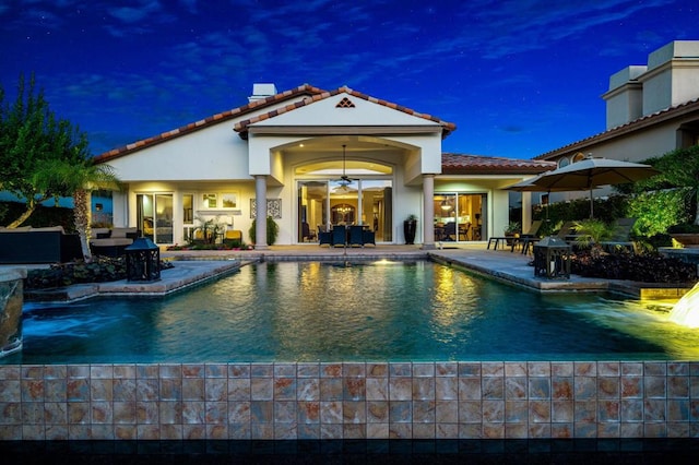 pool at night featuring a patio area and ceiling fan