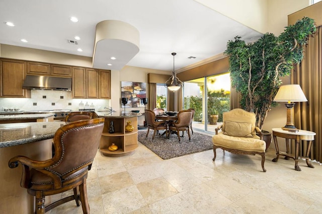 kitchen featuring dark stone counters, hanging light fixtures, a breakfast bar area, and backsplash