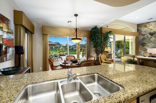 kitchen with sink, decorative light fixtures, a healthy amount of sunlight, and light stone countertops