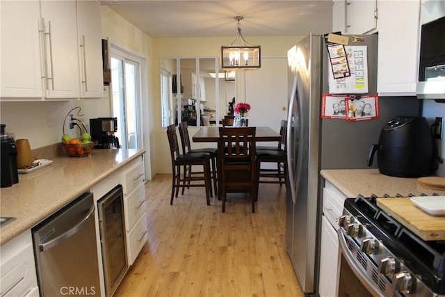 kitchen with appliances with stainless steel finishes, white cabinetry, a chandelier, light wood-type flooring, and decorative light fixtures