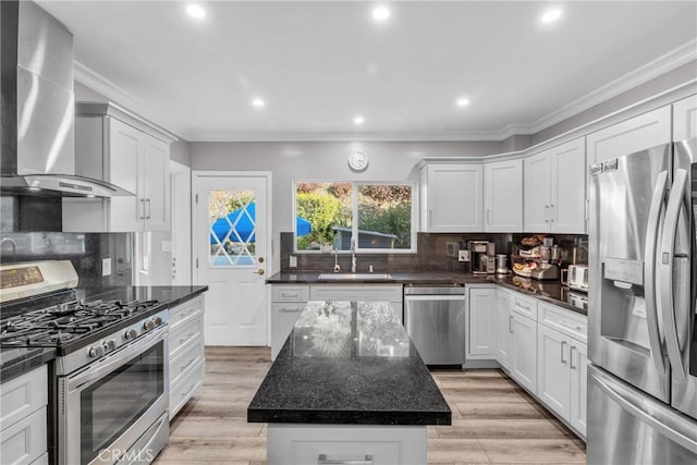 kitchen featuring a kitchen island, appliances with stainless steel finishes, white cabinetry, sink, and wall chimney range hood