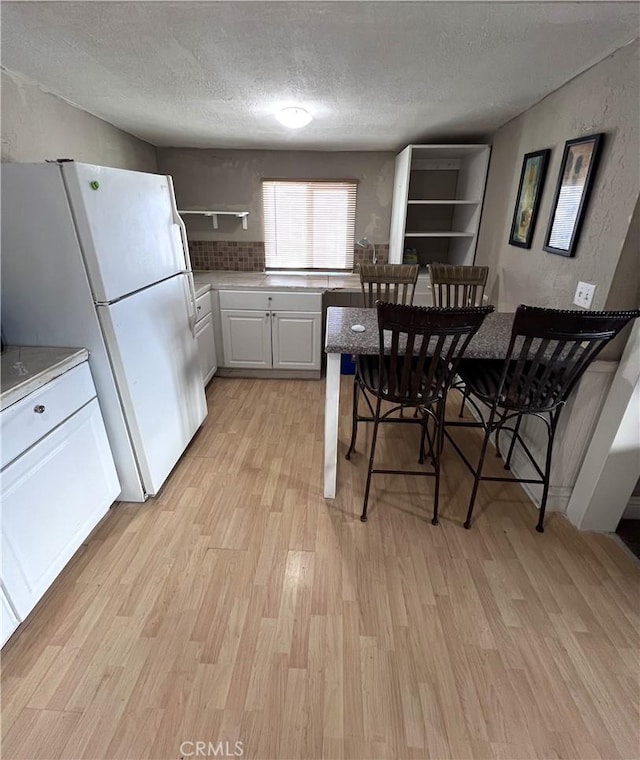 kitchen with white refrigerator, white cabinetry, a textured ceiling, and light wood-type flooring