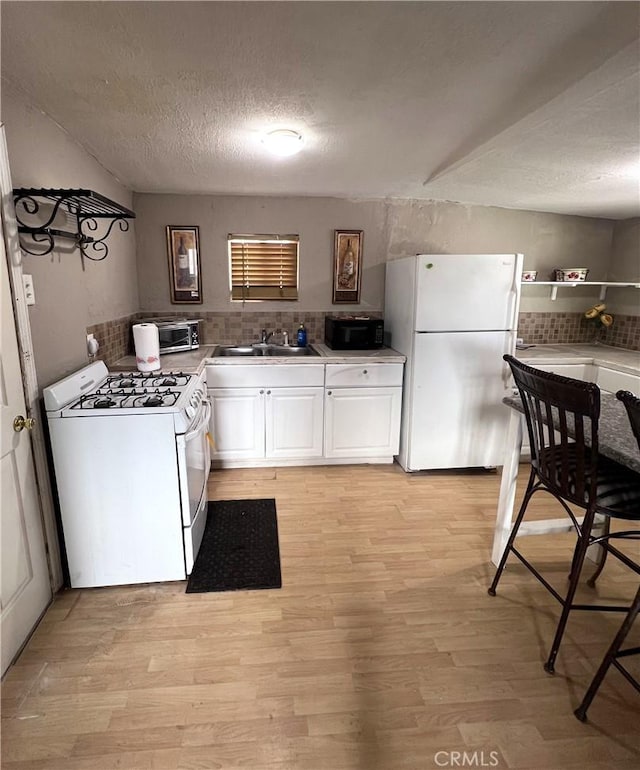 kitchen featuring white appliances, a textured ceiling, white cabinets, and light wood-type flooring