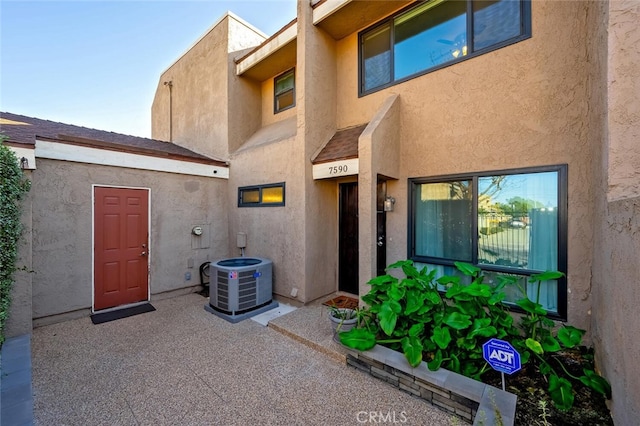 view of exterior entry featuring central AC unit and a patio